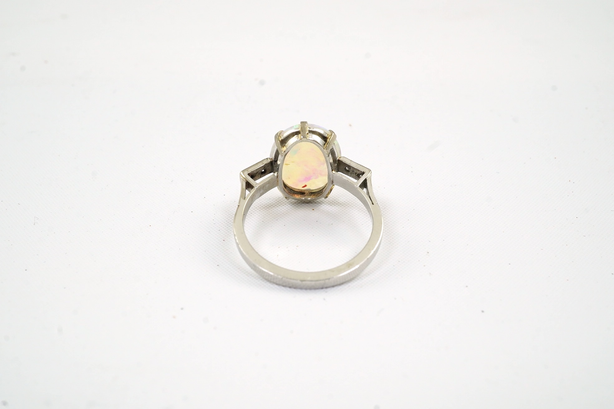 A white gold? and single stone oval cabochon opal set ring, with four stone diamond set shoulders